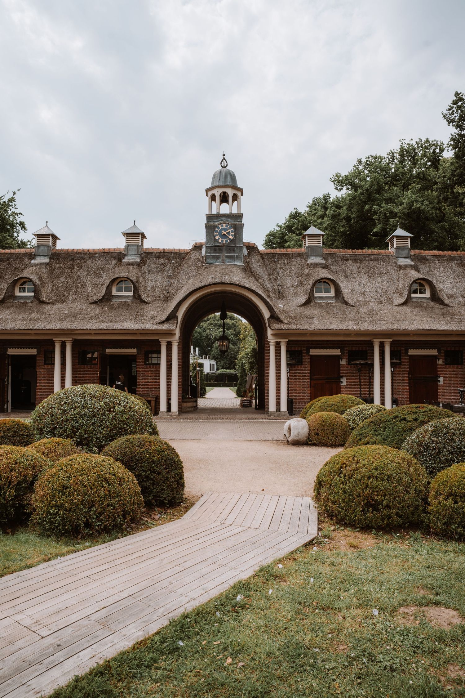 Historic brick stable building with arched entryways and clock tower under cloudy skies.