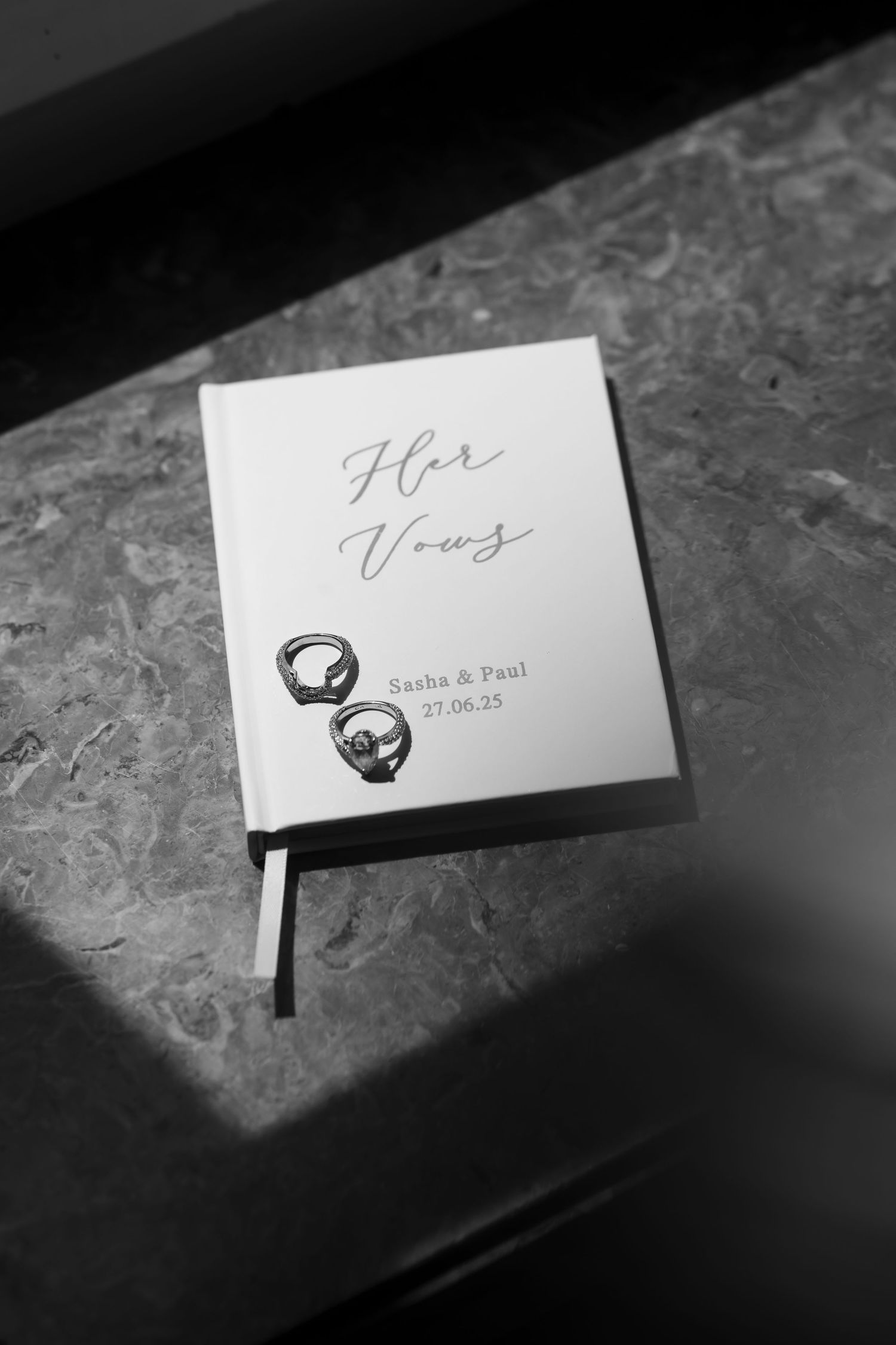 Black and white photograph of elegant wedding place cards with calligraphy names and ring designs on a textured surface.