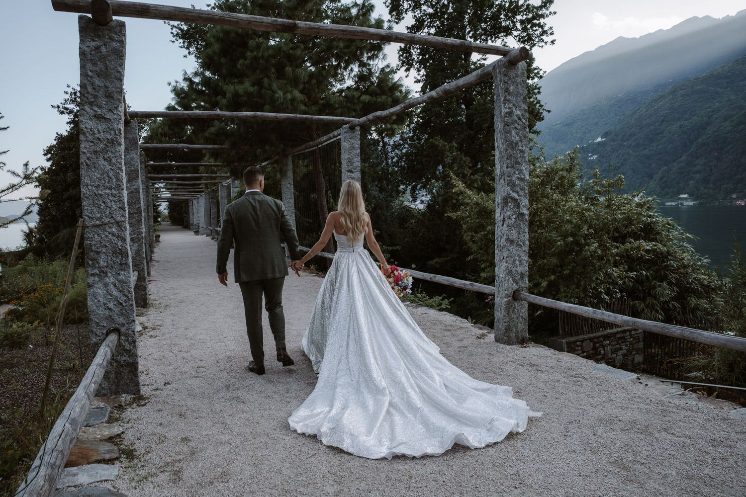 A couple in wedding attire walks along a scenic mountain path with stunning valley views in the background.