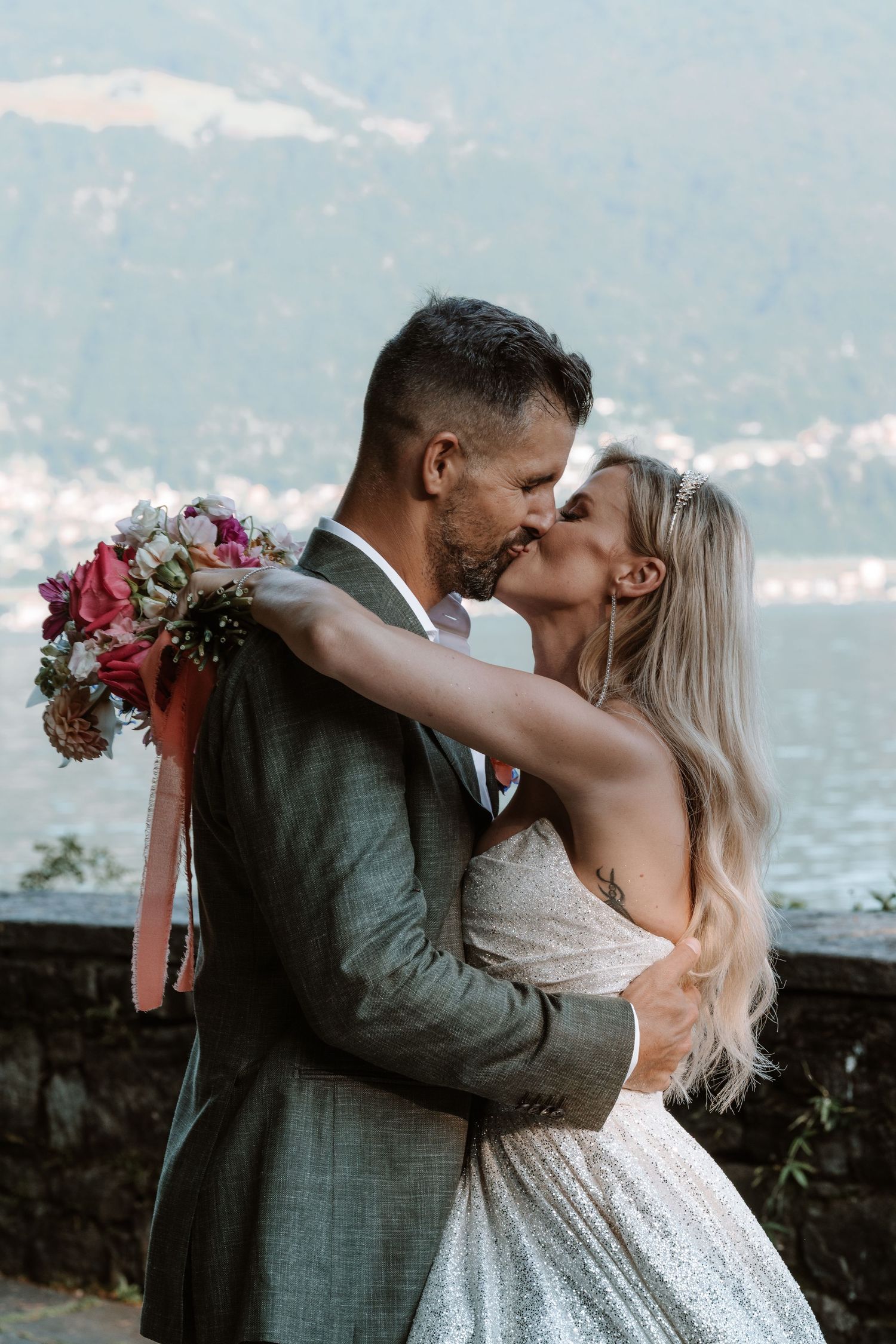 Romantic couple shares passionate kisses by a lakeside in a series of wedding photos with mountains in background.