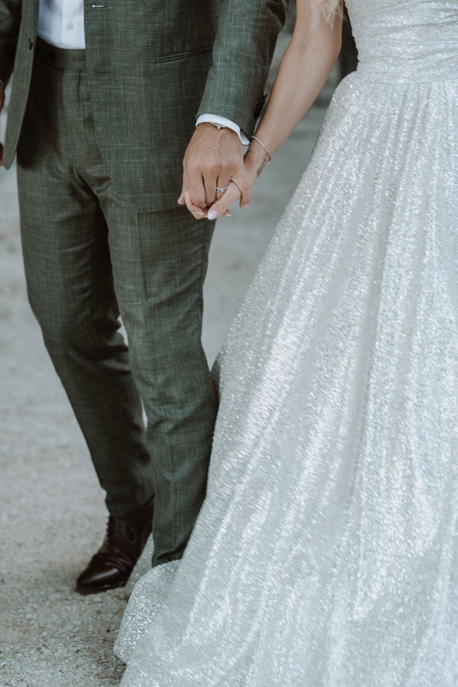Close-up detail of a couple holding hands, with the bride wearing a sparkly white gown and groom in dark suit.