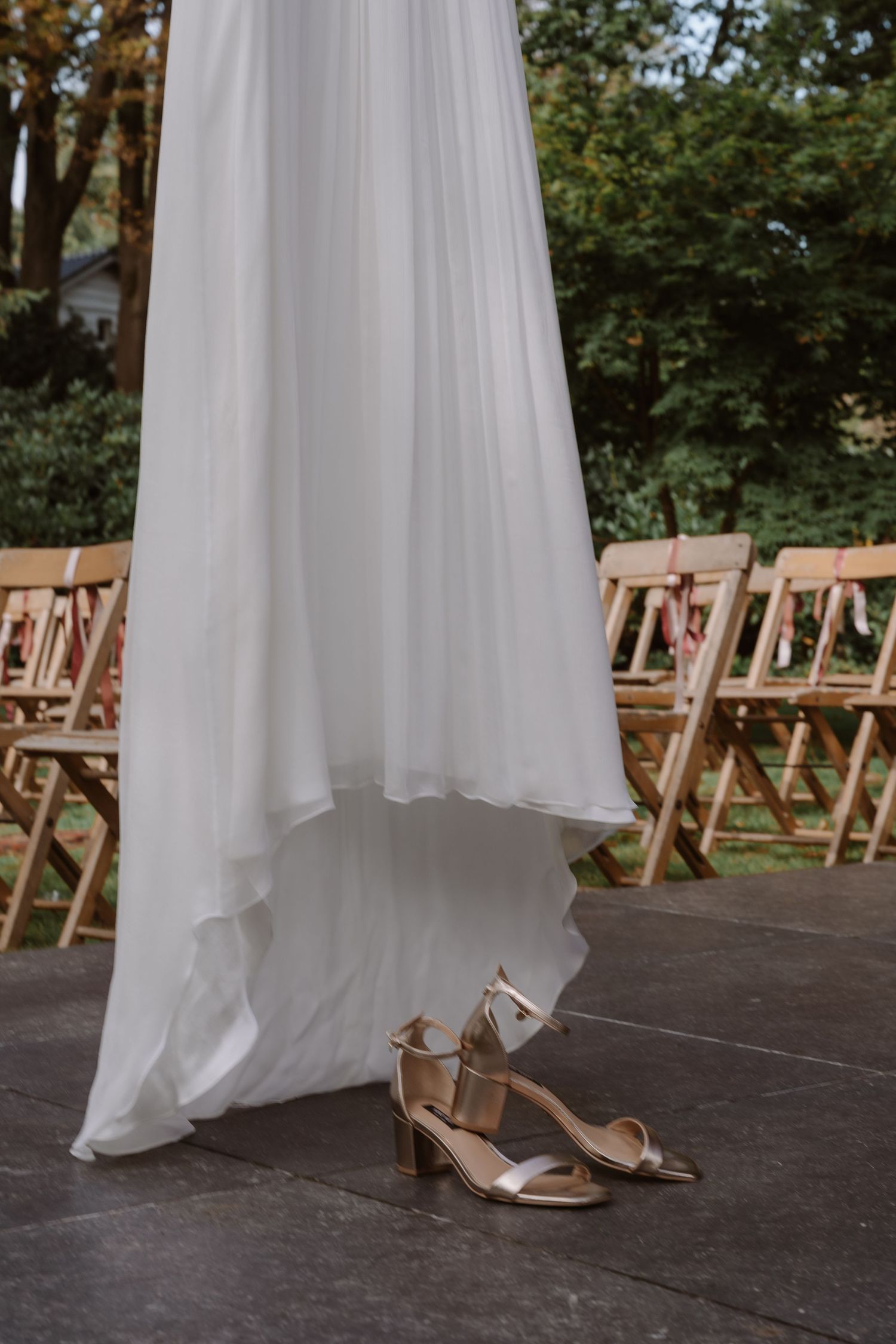 White wedding dress and silver heels displayed on a dark wooden floor.
