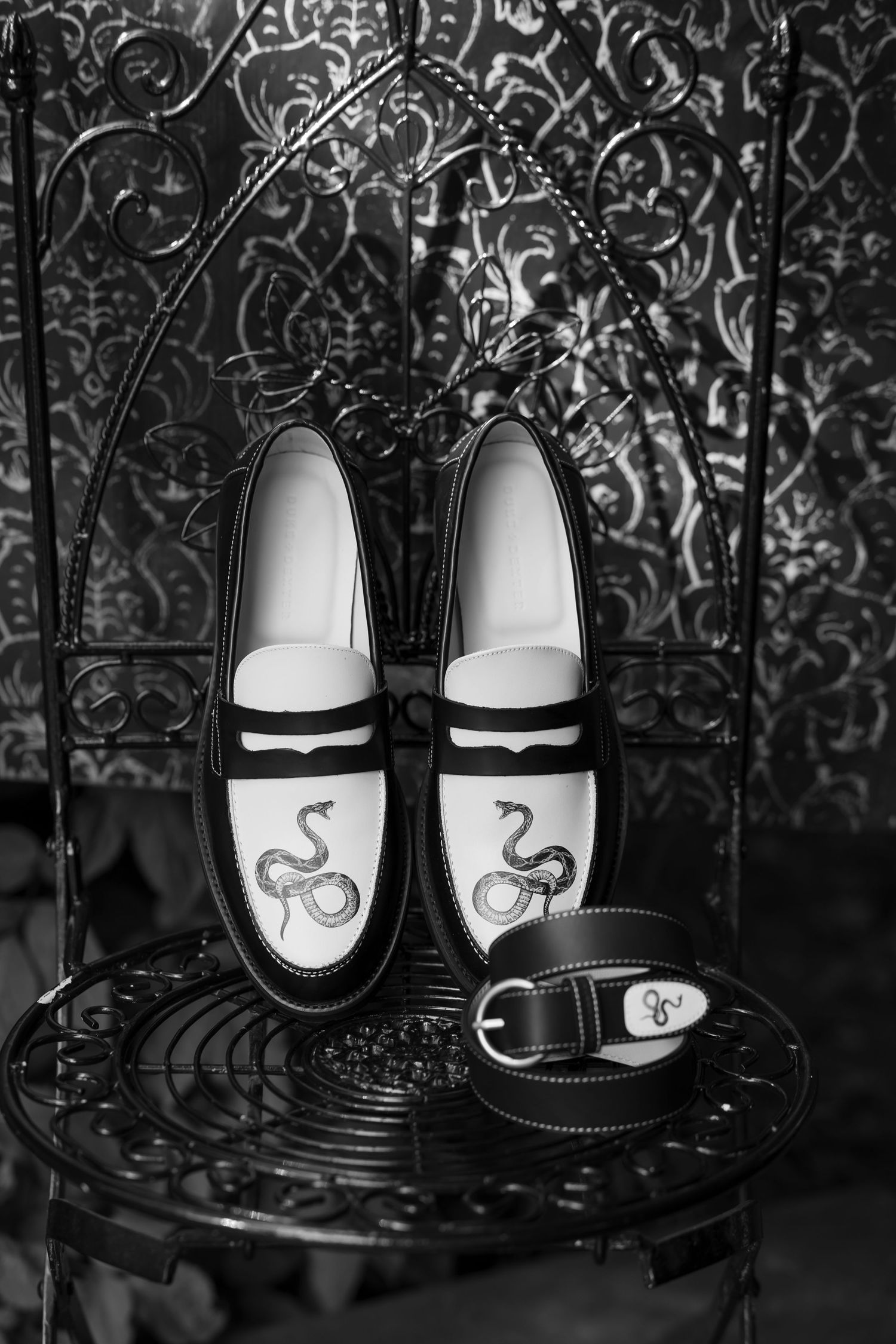 Black and white photo of matching bride and groom shoes with decorative ampersand designs.