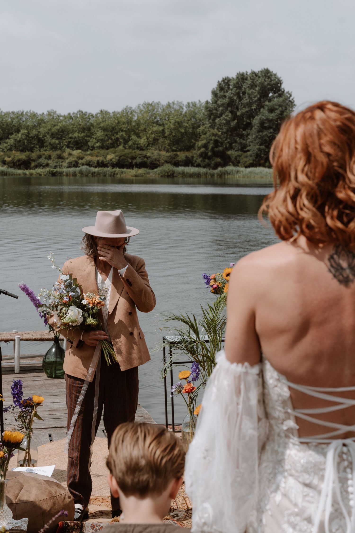 Wedding guests gather on a wooden dock overlooking a serene lake during an outdoor celebration.