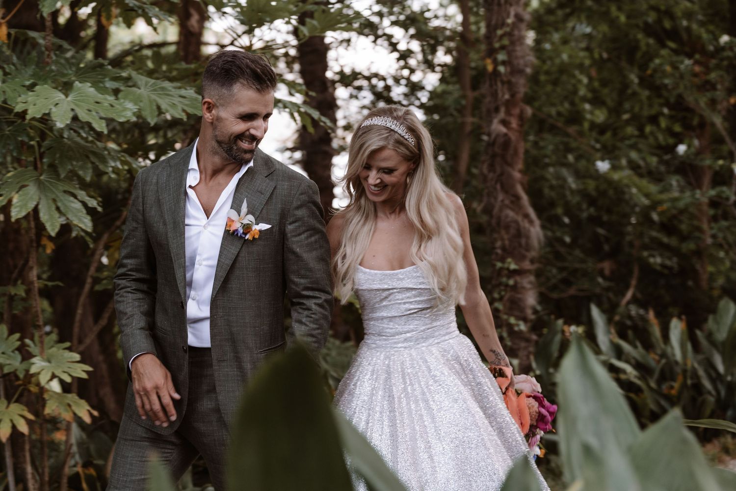 A couple shares a joyful moment together in a lush forest setting during their outdoor wedding celebration.