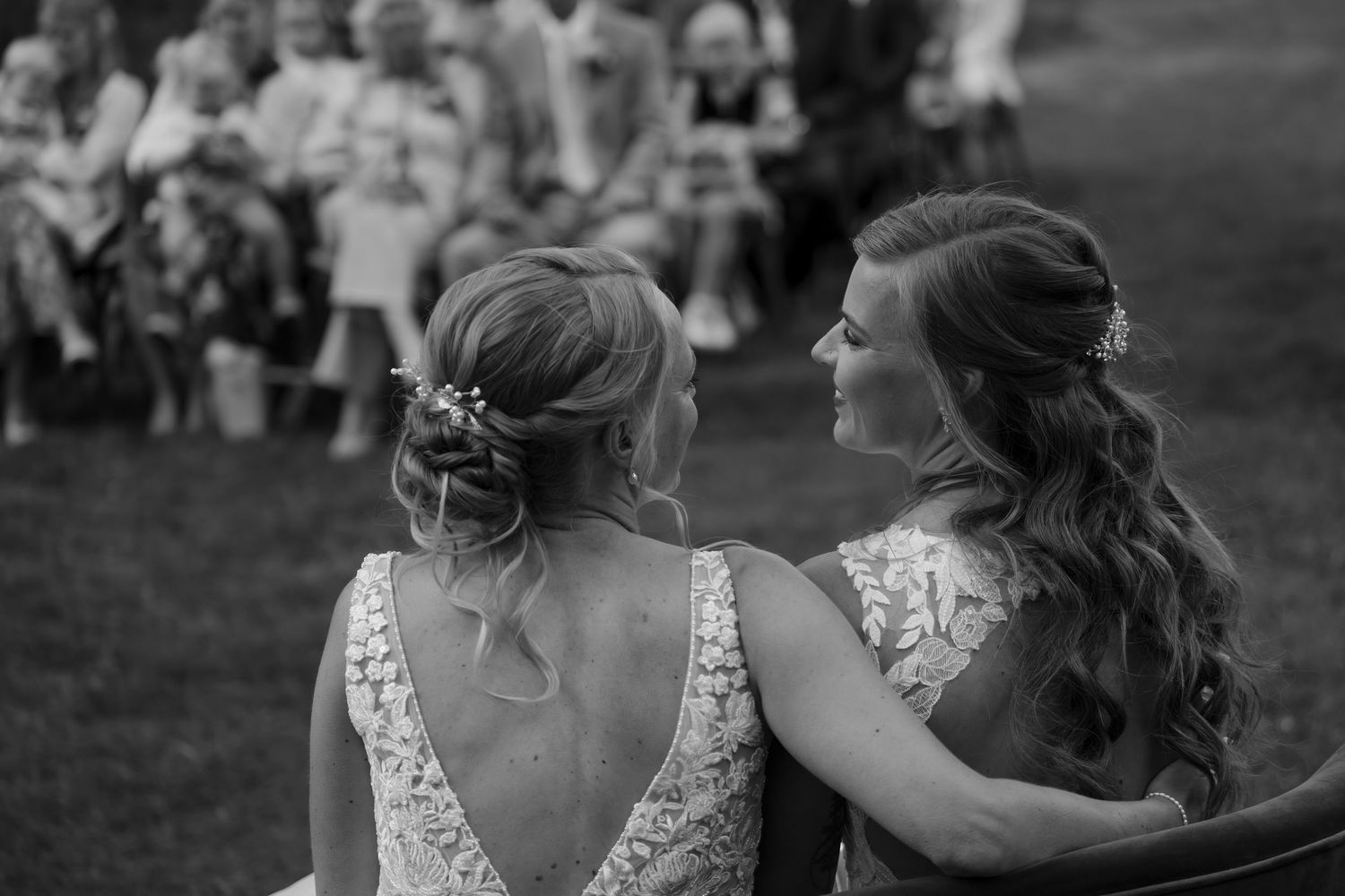 Black and white photo of two people in lace back wedding dresses sitting together.
