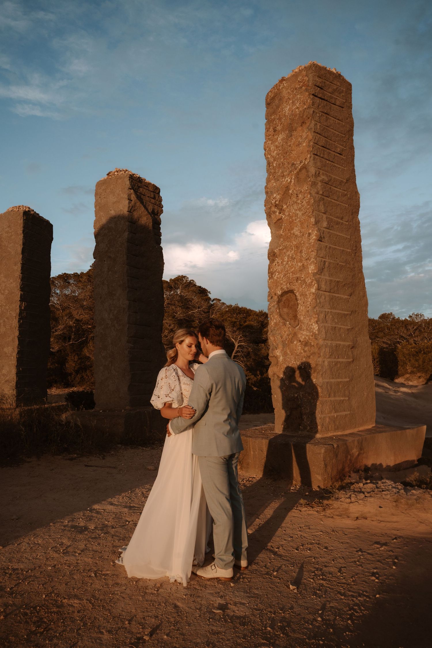 A romantic wedding photo shoot at ancient stone ruins during sunset creating a dramatic silhouette effect.
