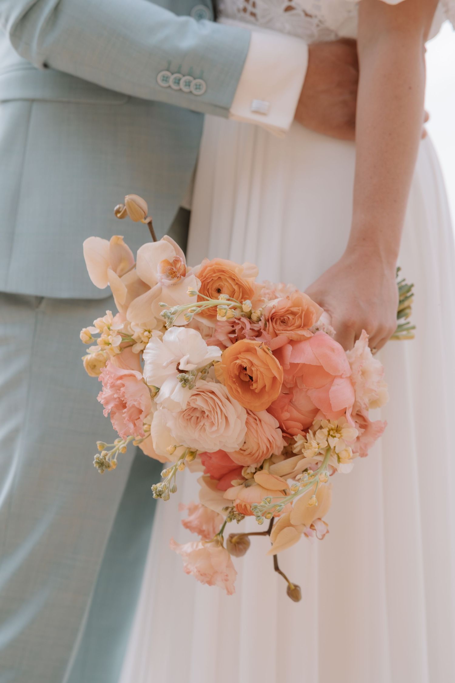 Delicate peach and pink bridal bouquet held against a light blue bridesmaid dress.