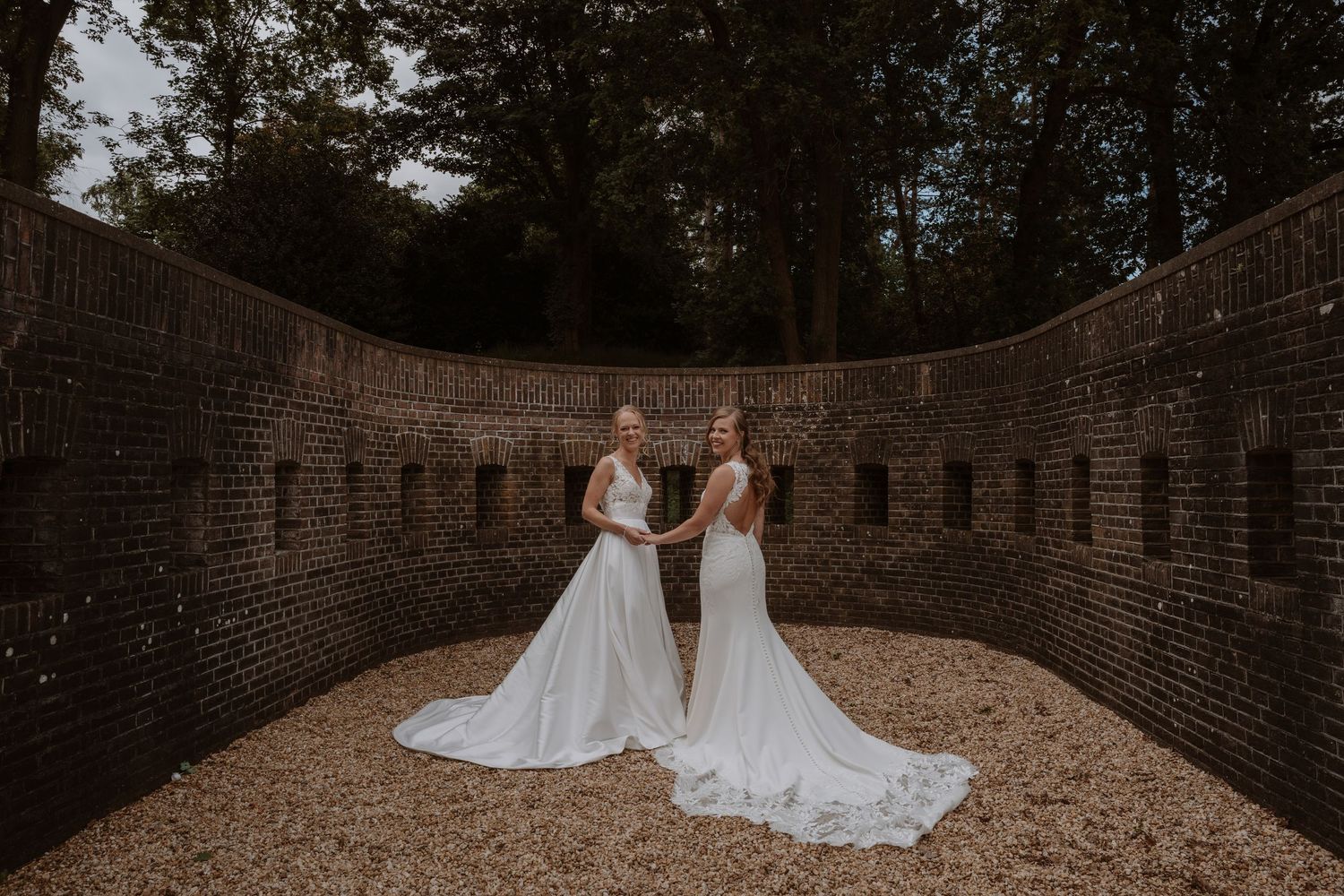 Two wedding dresses photographed in romantic courtyard setting with brick walls.