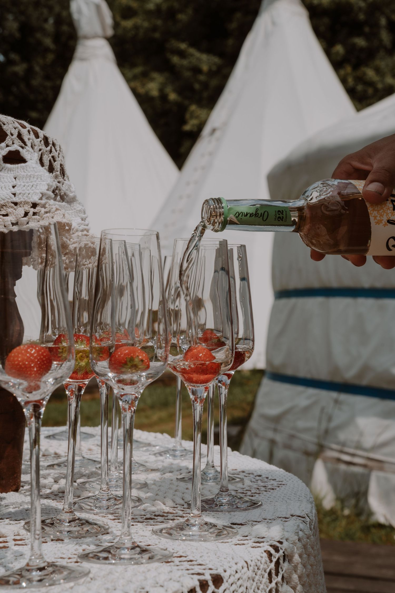Wine glasses being filled on a white lace tablecloth at an outdoor event.