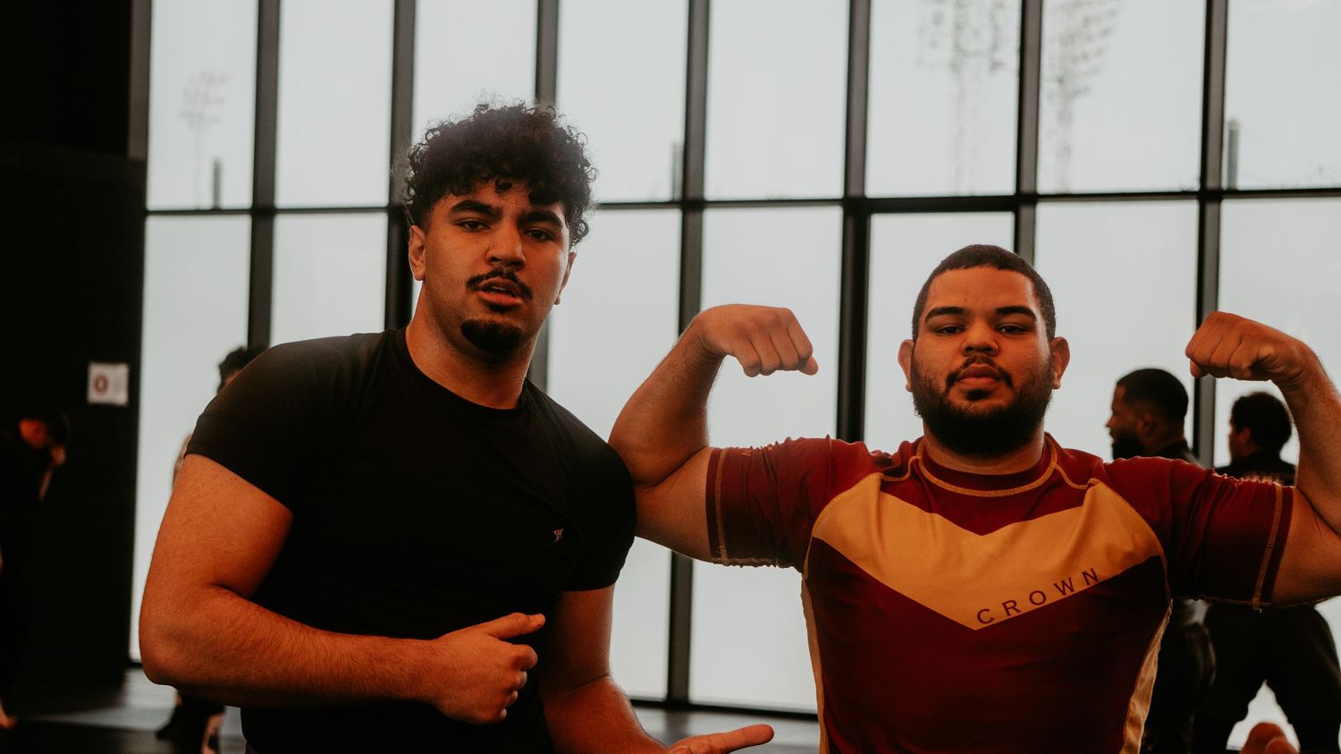 Two male athletes posing together and flexing in a martial arts gym setting