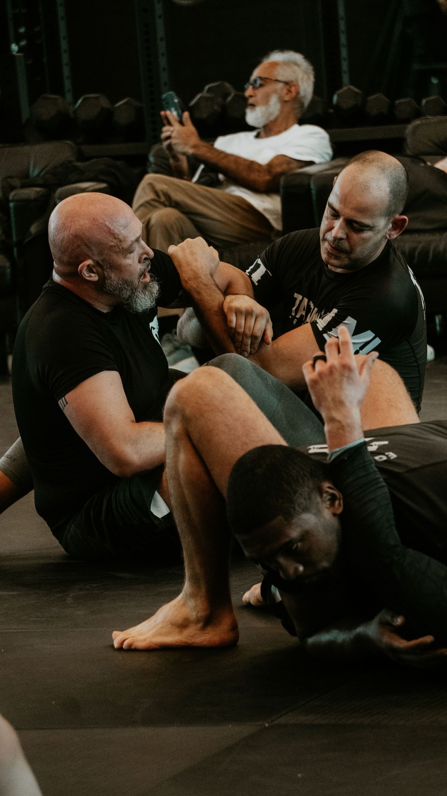 Three BJJ athletes practicing ground grappling techniques during a martial arts training session