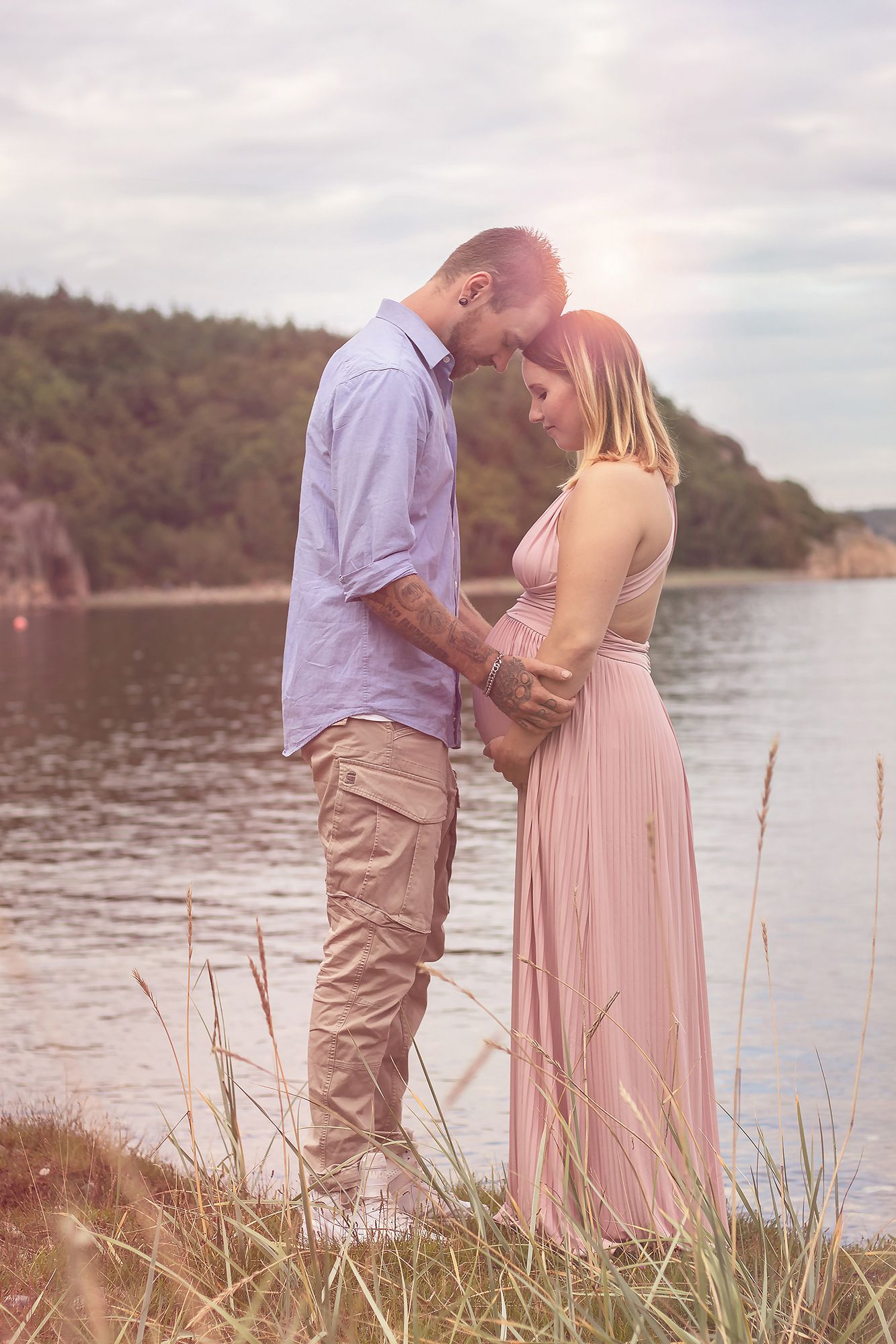 Sagolik fotografering på gravid kvinna med make vid strandkanten i Åbyfjorden, mjukt naturligt ljus i solnedgång utanför Göteborg.