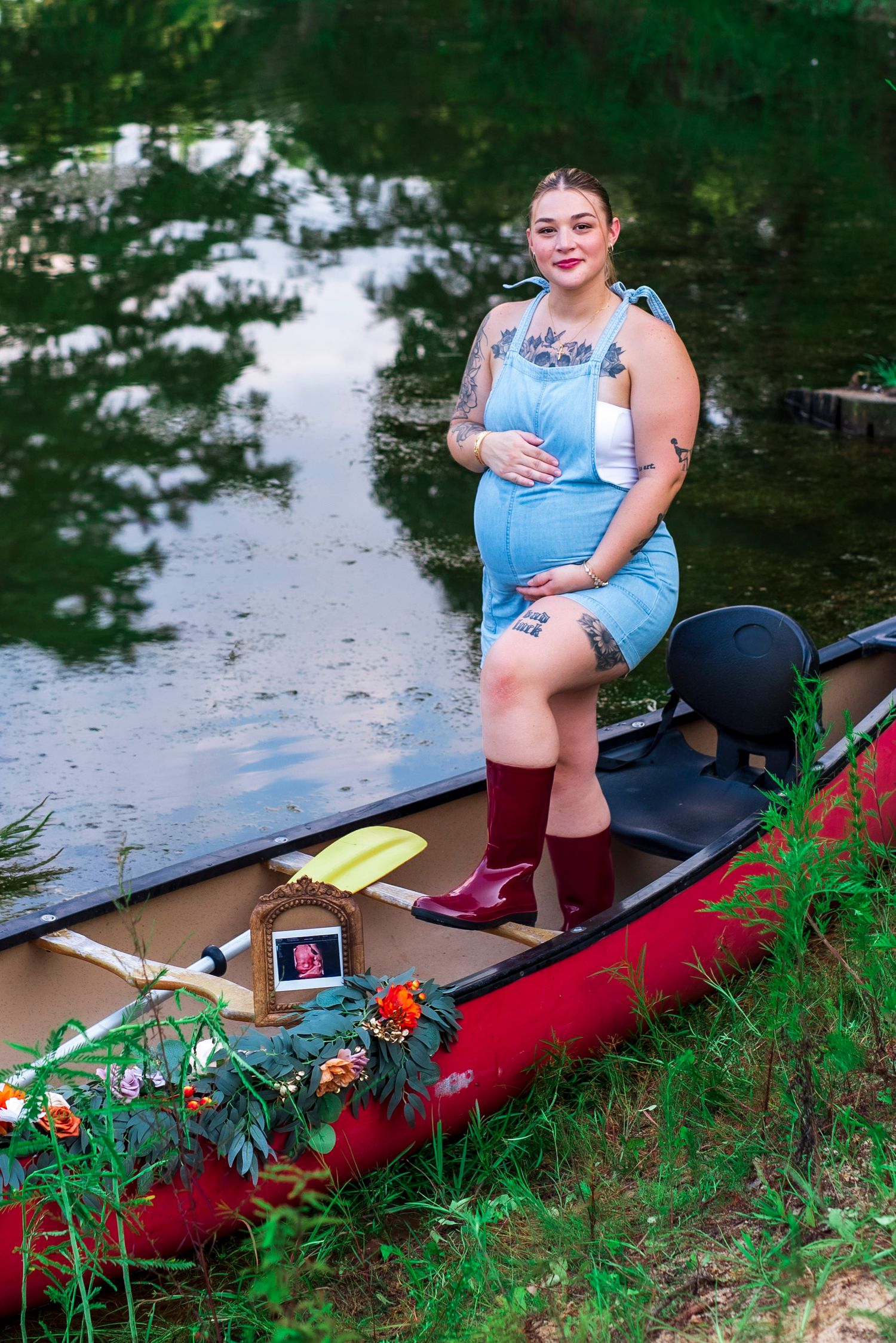 Expectant mother standing in a canoe and gently cradling her baby bump during an outdoor maternity photography session.