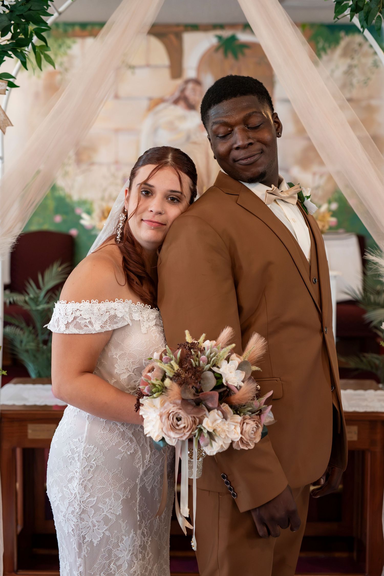 Newlywed couple embracing beneath a soft draped wedding arch during an intimate wedding ceremony.