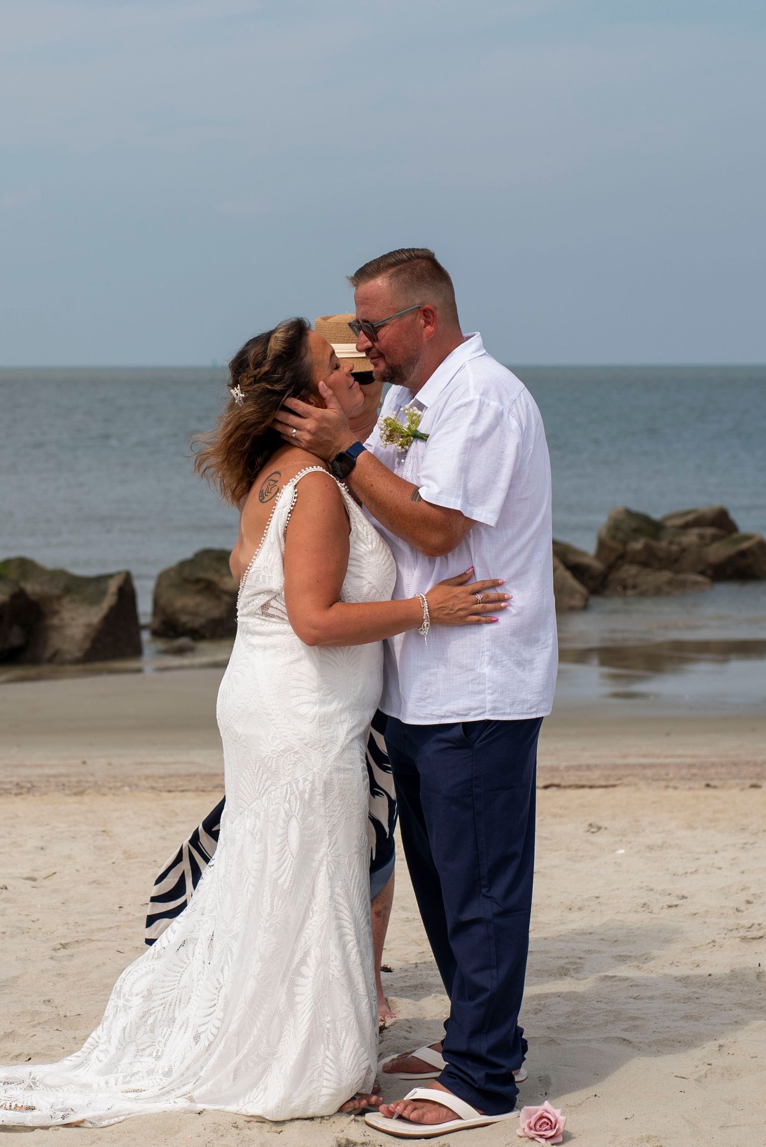 Bride and groom sharing a kiss on the beach with the ocean and rocky shoreline behind them.