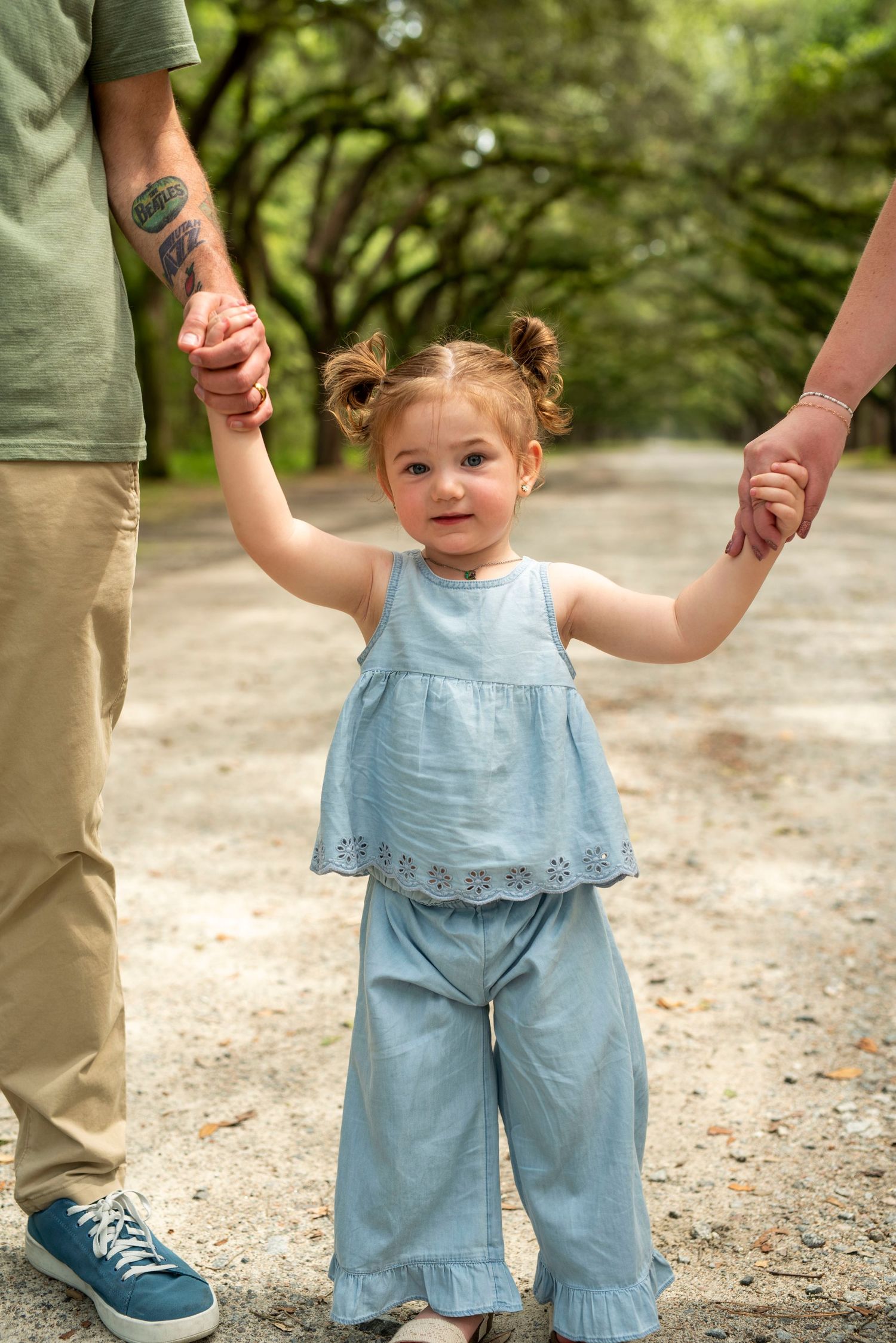 Toddler holding parents’ hands while beneath the iconic oak trees at Wormsloe Historic Site in Savannah, Georgia, during a family session.