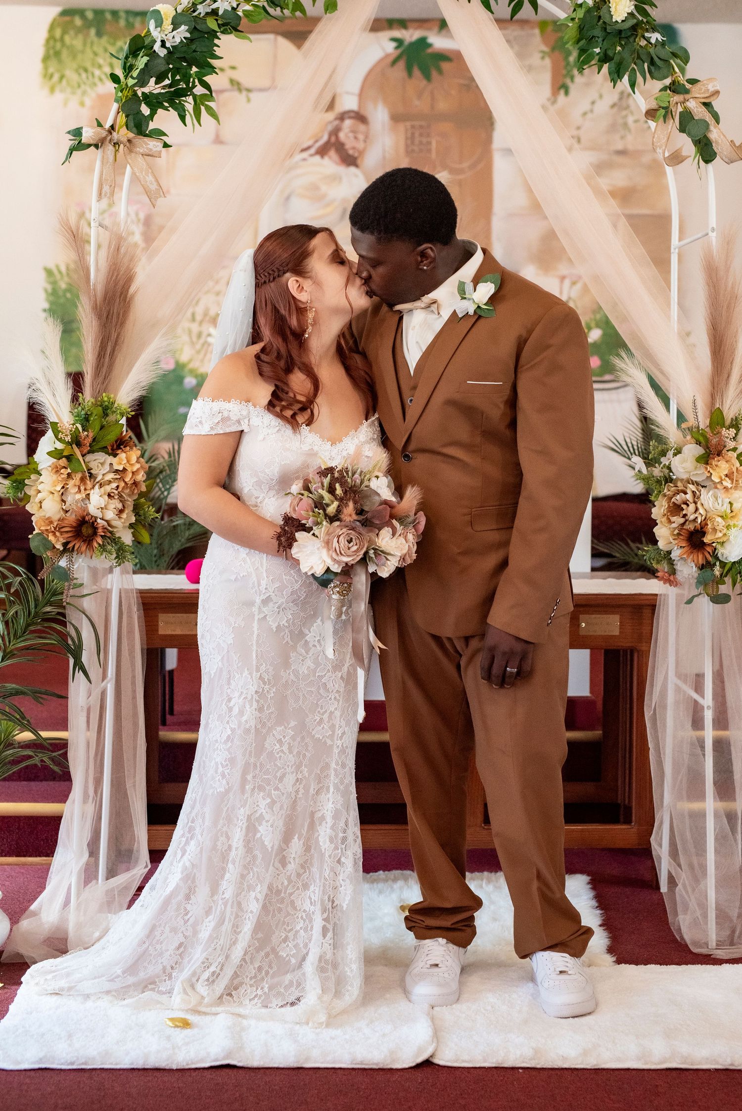 Newlywed couple embracing beneath a softly draped wedding arch after an intimate wedding ceremony.