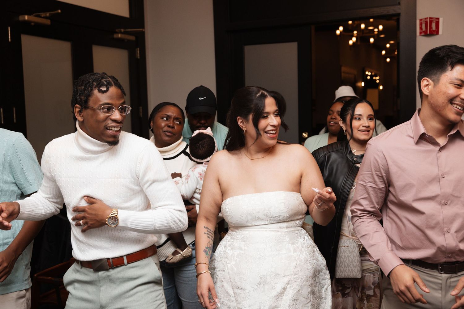 Joyful bride in strapless white gown dancing with groom and guests at lively wedding reception.