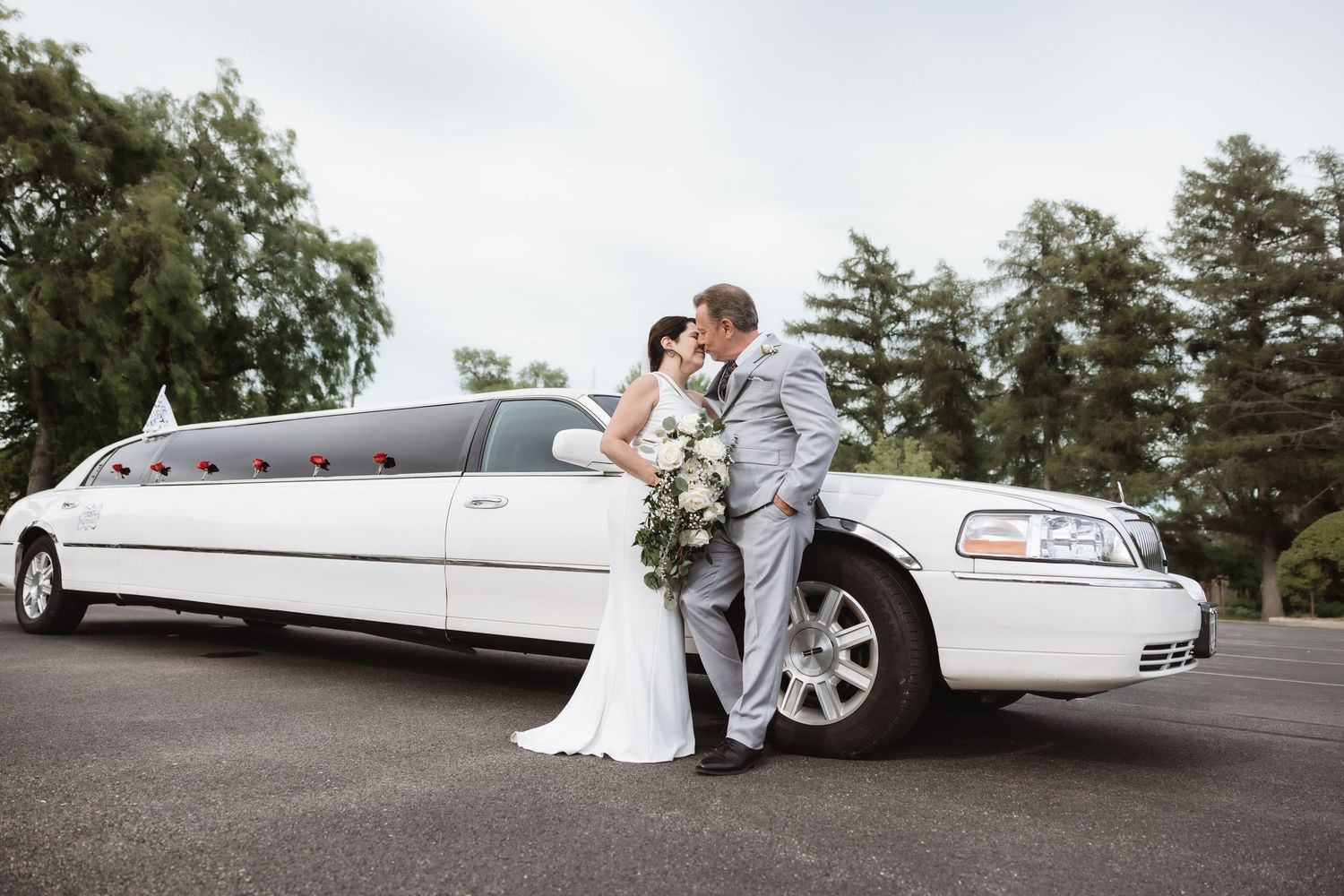 Bride and groom share a romantic kiss beside a white stretch limousine on their wedding day.