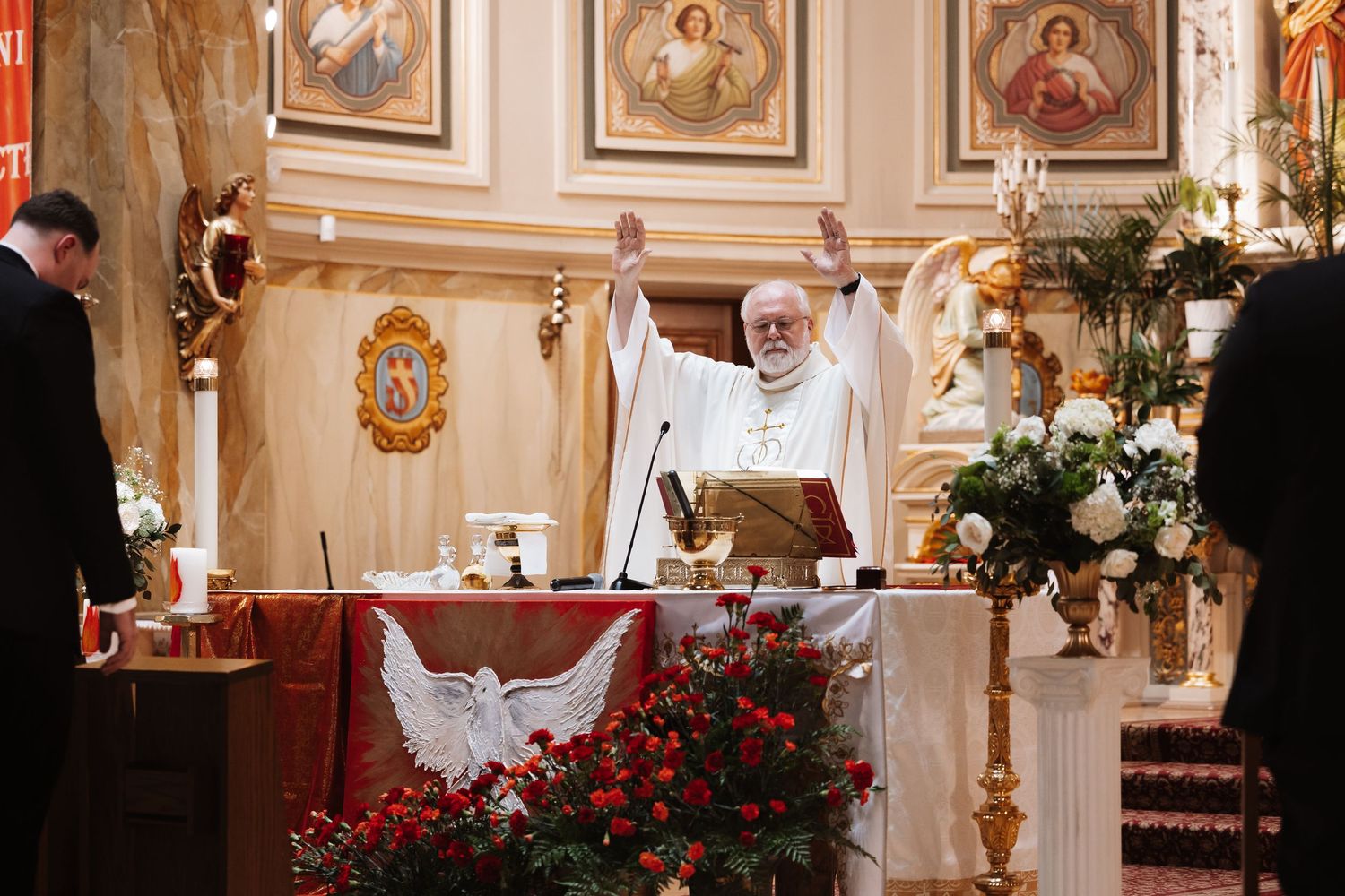 Catholic priest raises hands in blessing at ornate golden altar during wedding Mass ceremony.