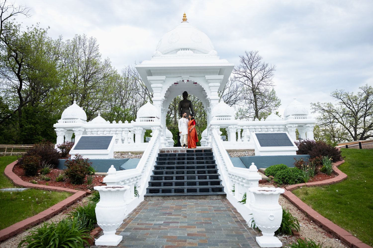 Indian couple in traditional wedding attire standing at the entrance of a white Hindu temple.