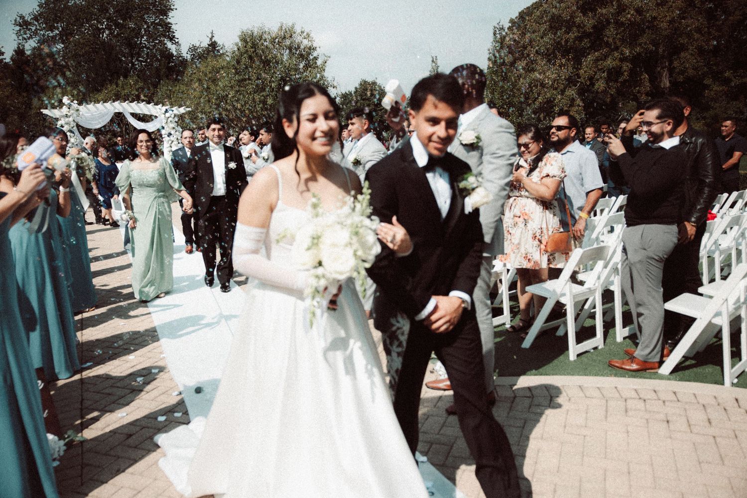 Newlywed couple walking joyfully down the aisle after their outdoor wedding ceremony surrounded by guests.