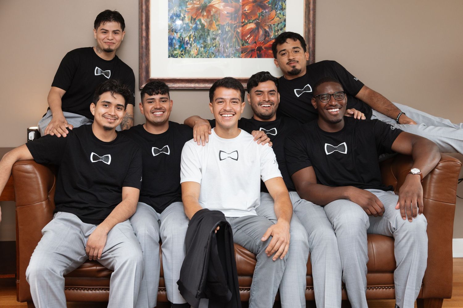 Groom and groomsmen posing together on leather sofa wearing matching black t-shirts with bow tie design.