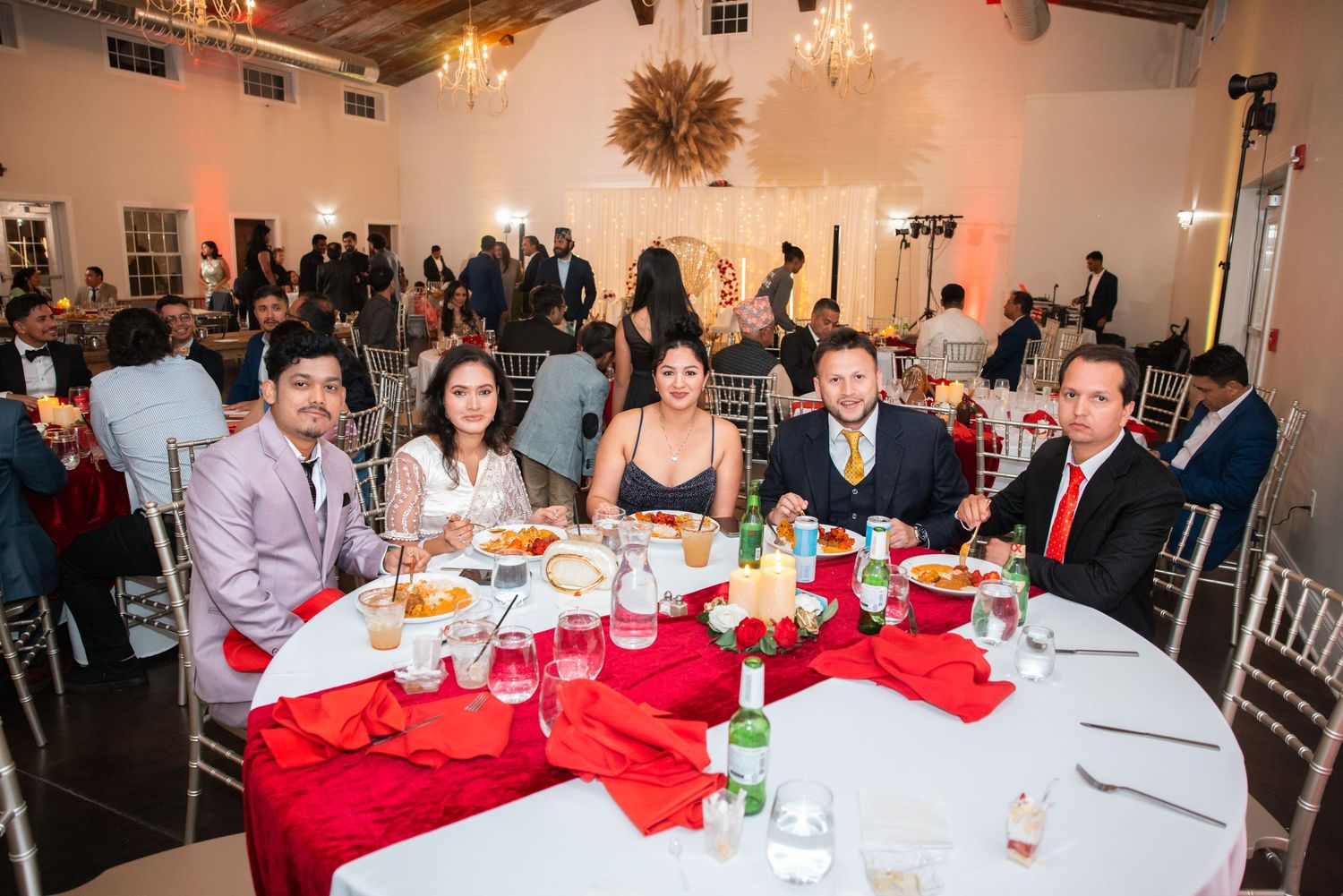 Group of five guests smiling at a festive banquet table with red napkins at an elegant event.