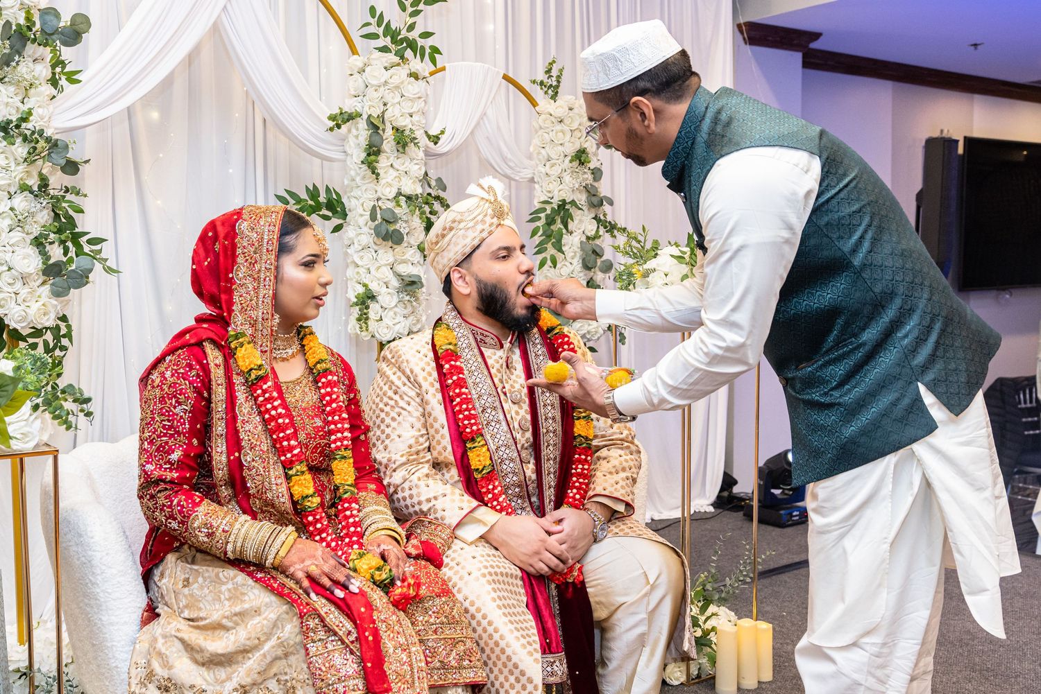 Traditional South Asian wedding ceremony with bride and groom in ornate red and gold attire receiving blessings.
