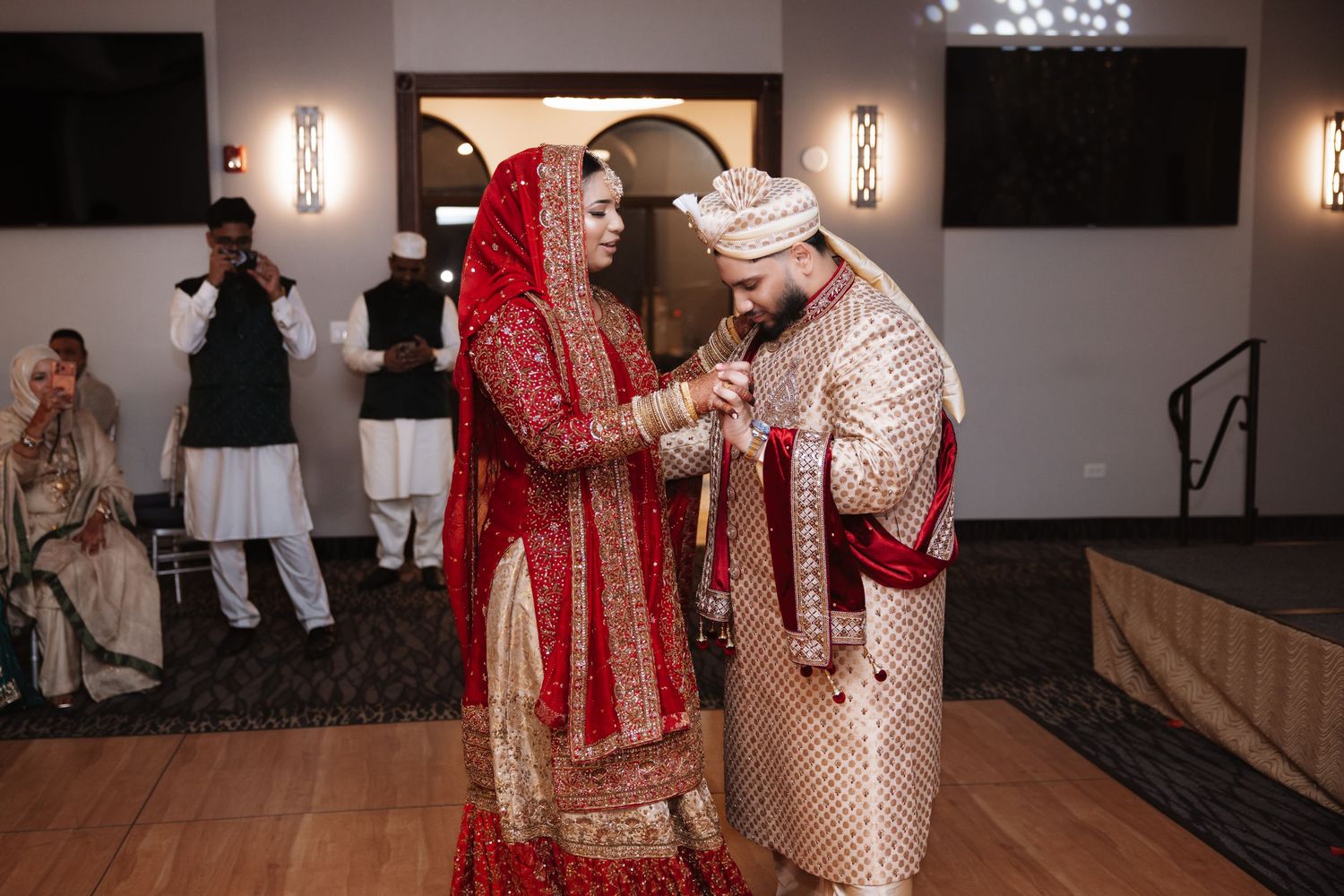 South Asian bride and groom exchange rings in traditional red and gold wedding attire.