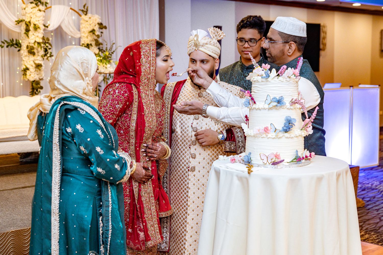 Wedding guests in traditional South Asian attire cutting a decorated cake.