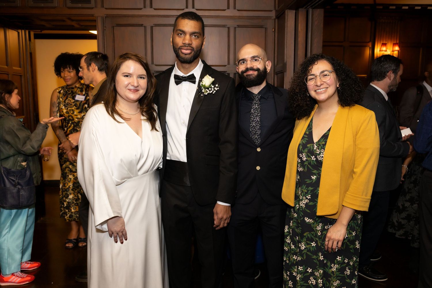 Bride and groom in tuxedo pose with two guests at wedding reception.