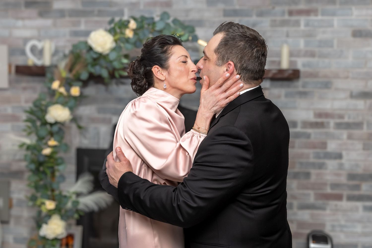 Newlyweds embrace in romantic first kiss in front of elegant floral fireplace wedding backdrop.