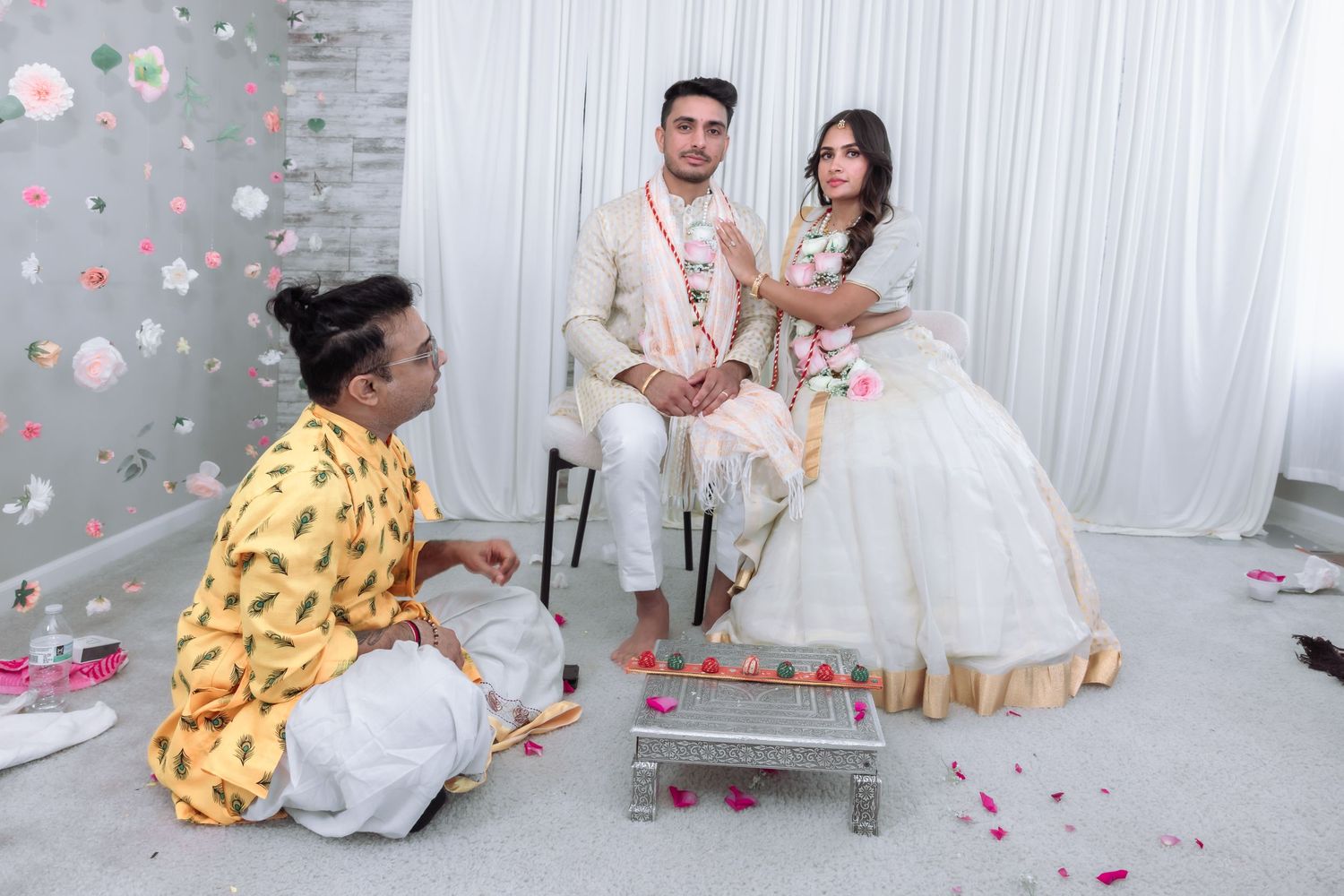 Indian bride and groom seated during traditional Hindu wedding ceremony with priest performing rituals.