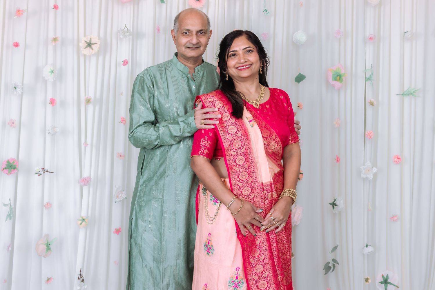Indian couple posing together at celebration, man in green kurta, woman in pink saree.