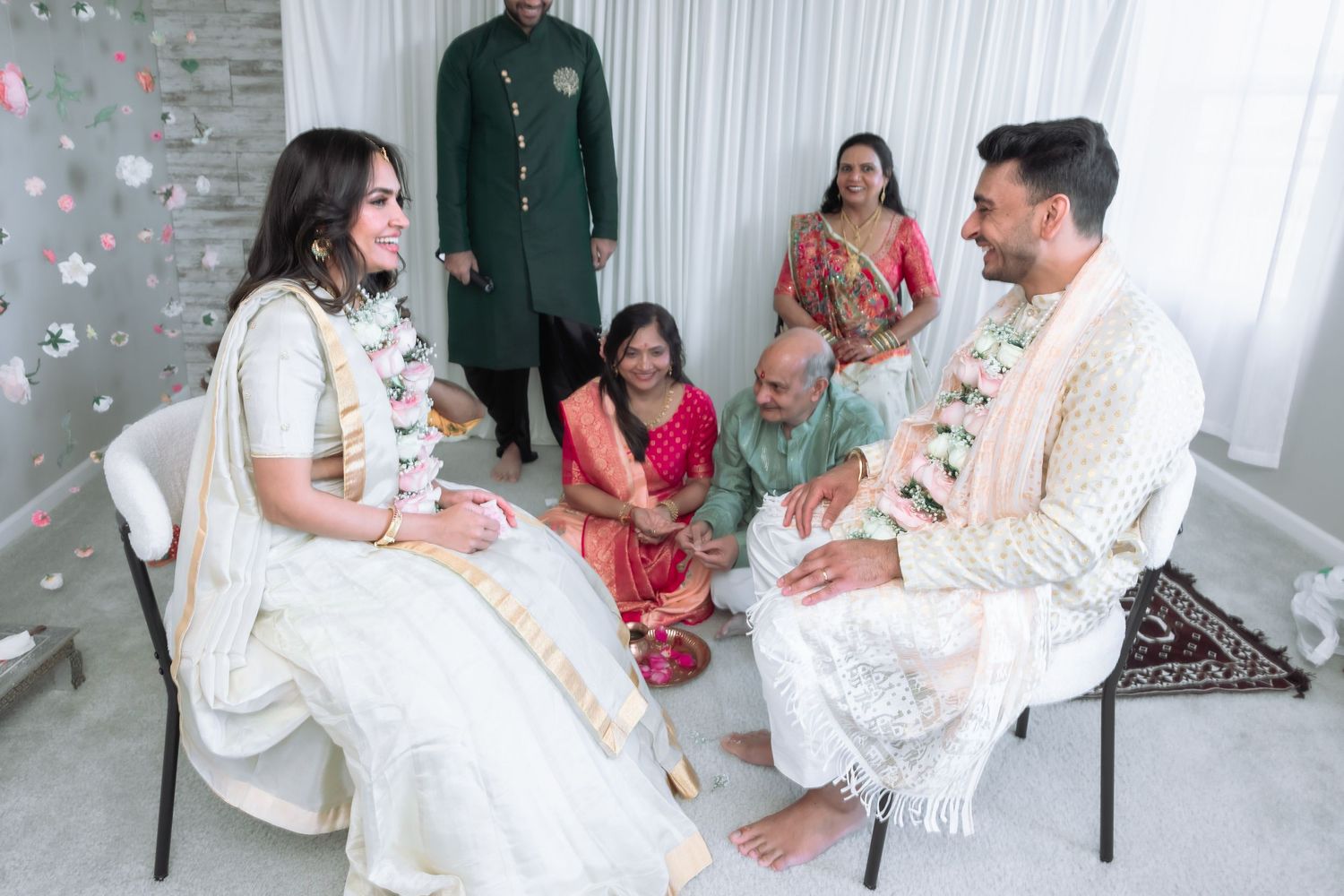 South Asian wedding ceremony with bride in white lehenga and groom in cream sherwani seated with family.