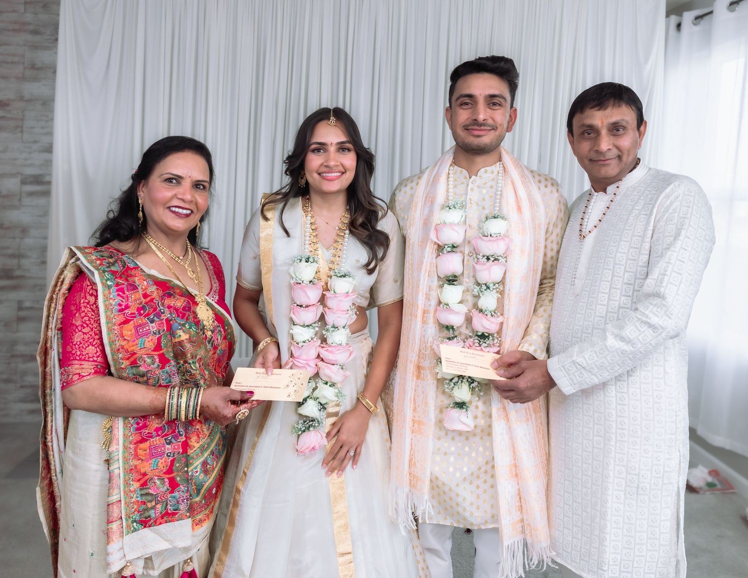 Two couples exchanging gifts at Indian engagement ceremony wearing floral garlands.