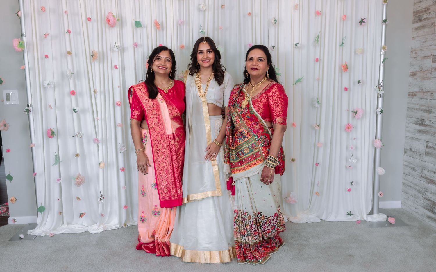 Three Indian women posing together in traditional attire at a wedding celebration.