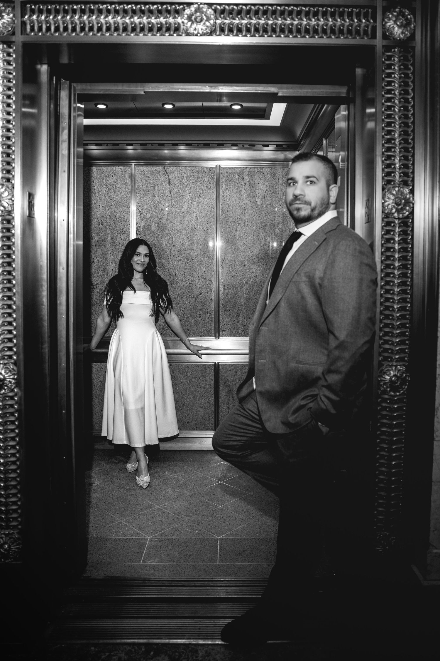 Bride and groom posing in elegant gold elevator in black and white wedding photo.