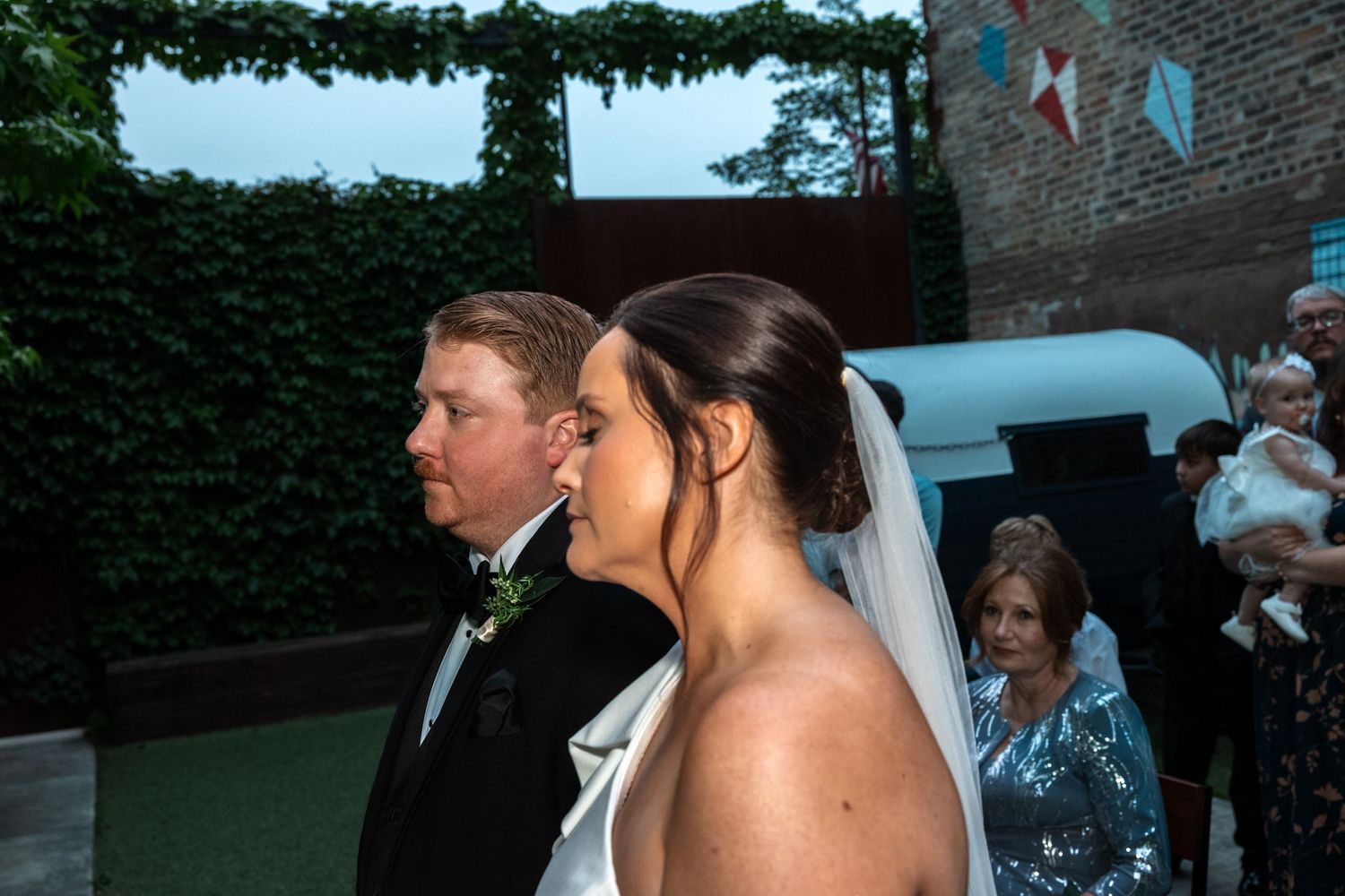 Bride and groom stand side by side in profile during their outdoor evening wedding reception.