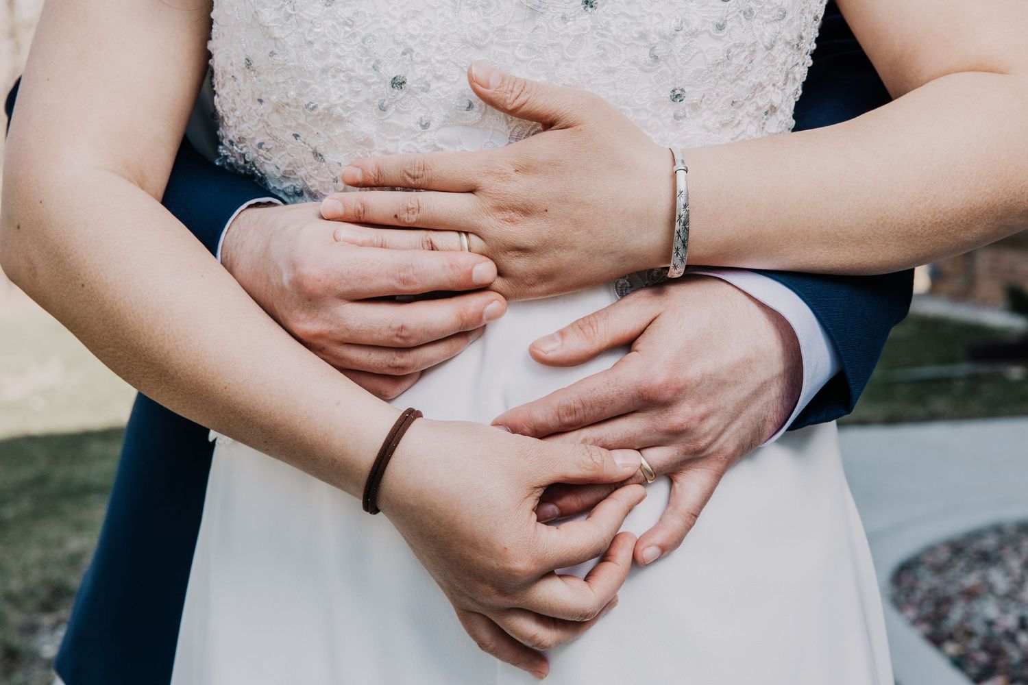Detail shot of bride and groom hands with wedding rings embracing at outdoor wedding ceremony.