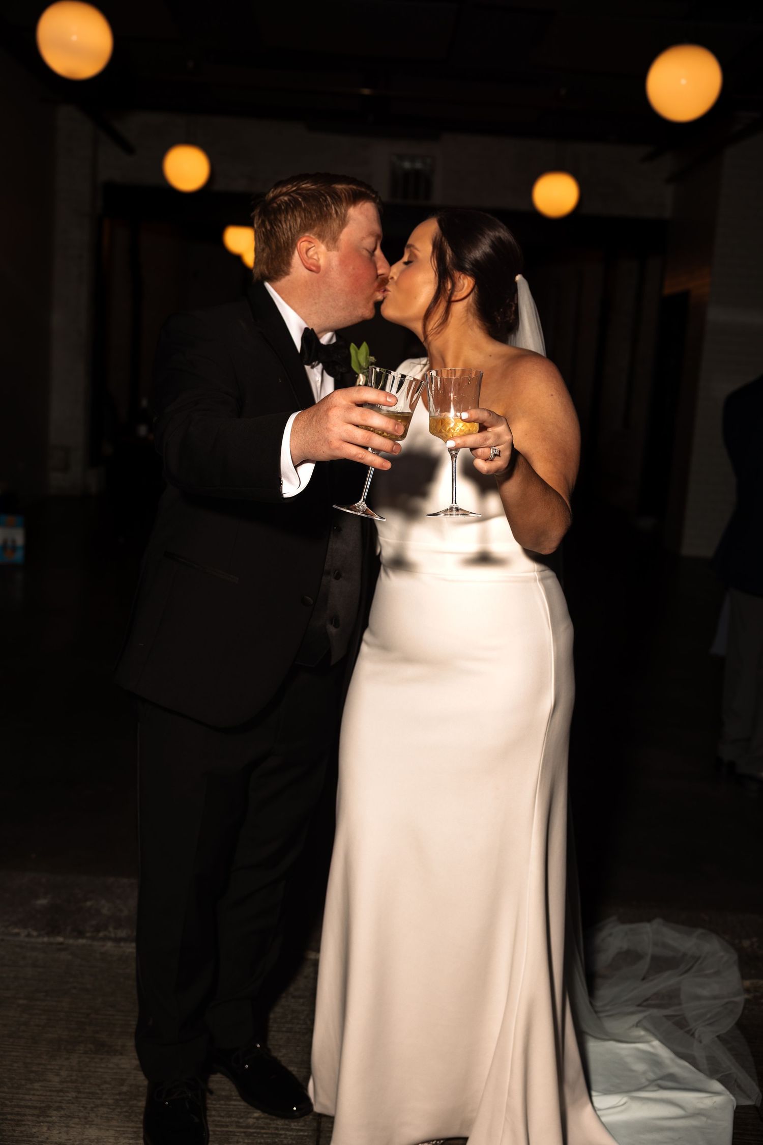 Bride and groom sharing a kiss while holding champagne glasses at their wedding.