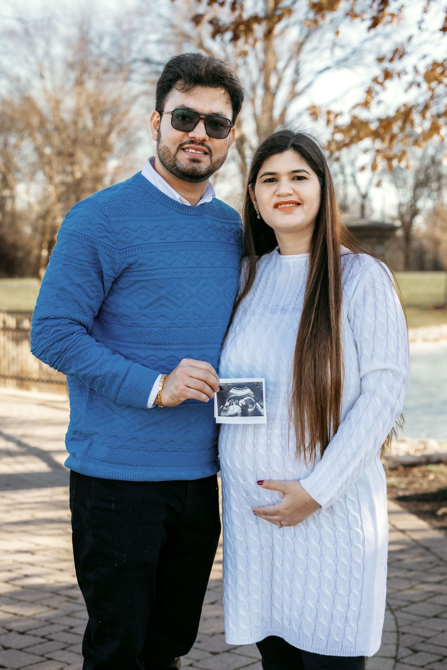 Smiling couple holding ultrasound image during outdoor maternity photoshoot in autumn park.