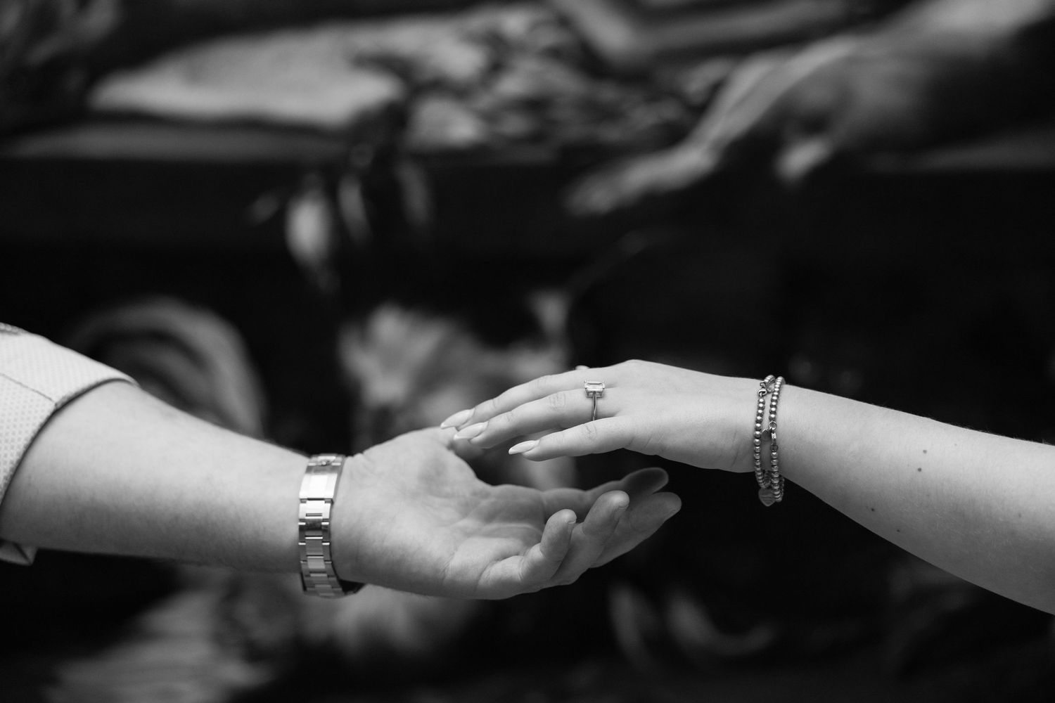 Black and white photo of two hands gently touching, adorned with bracelets and a ring.