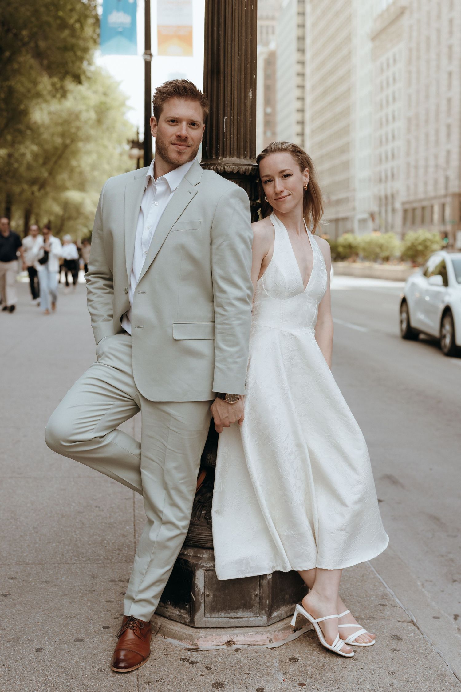 Bride and groom in neutral tones pose back-to-back against a city street lamp post.
