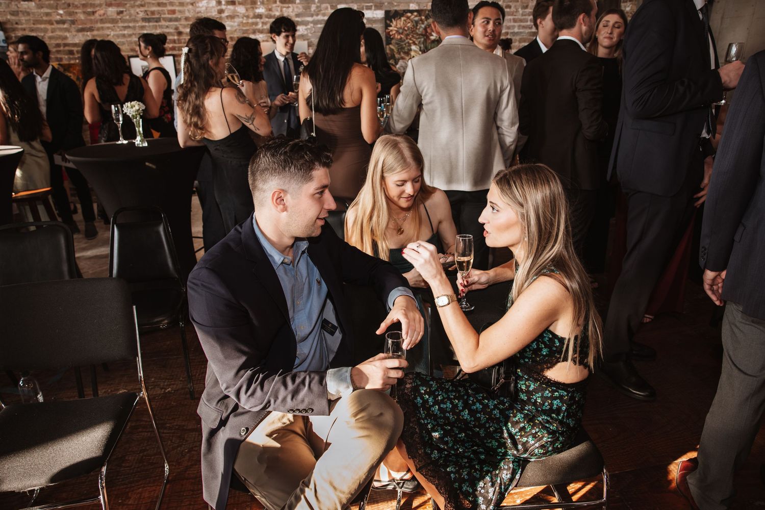 Couple in evening attire share an intimate conversation at a dimly lit upscale social gathering.