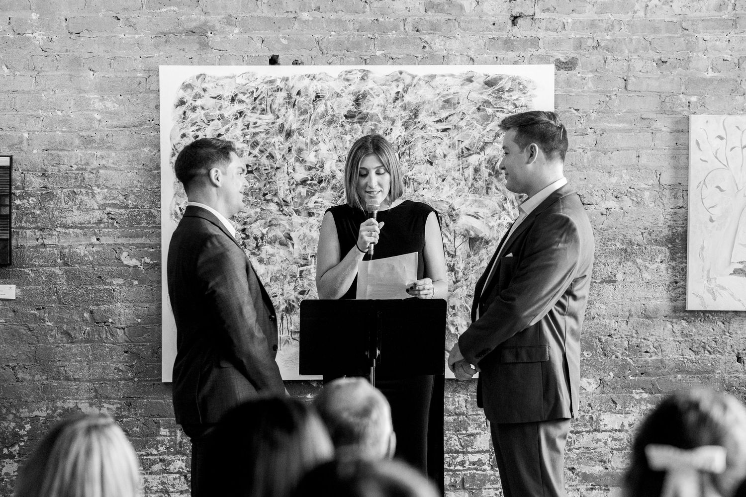 Black and white photo of wedding officiant reading vows to couple in gallery.
