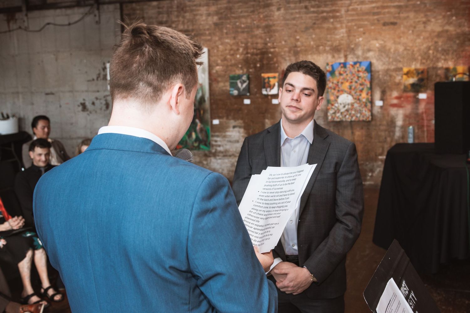 Groom holding ceremony papers exchanges vows with partner during intimate wedding in an art gallery.