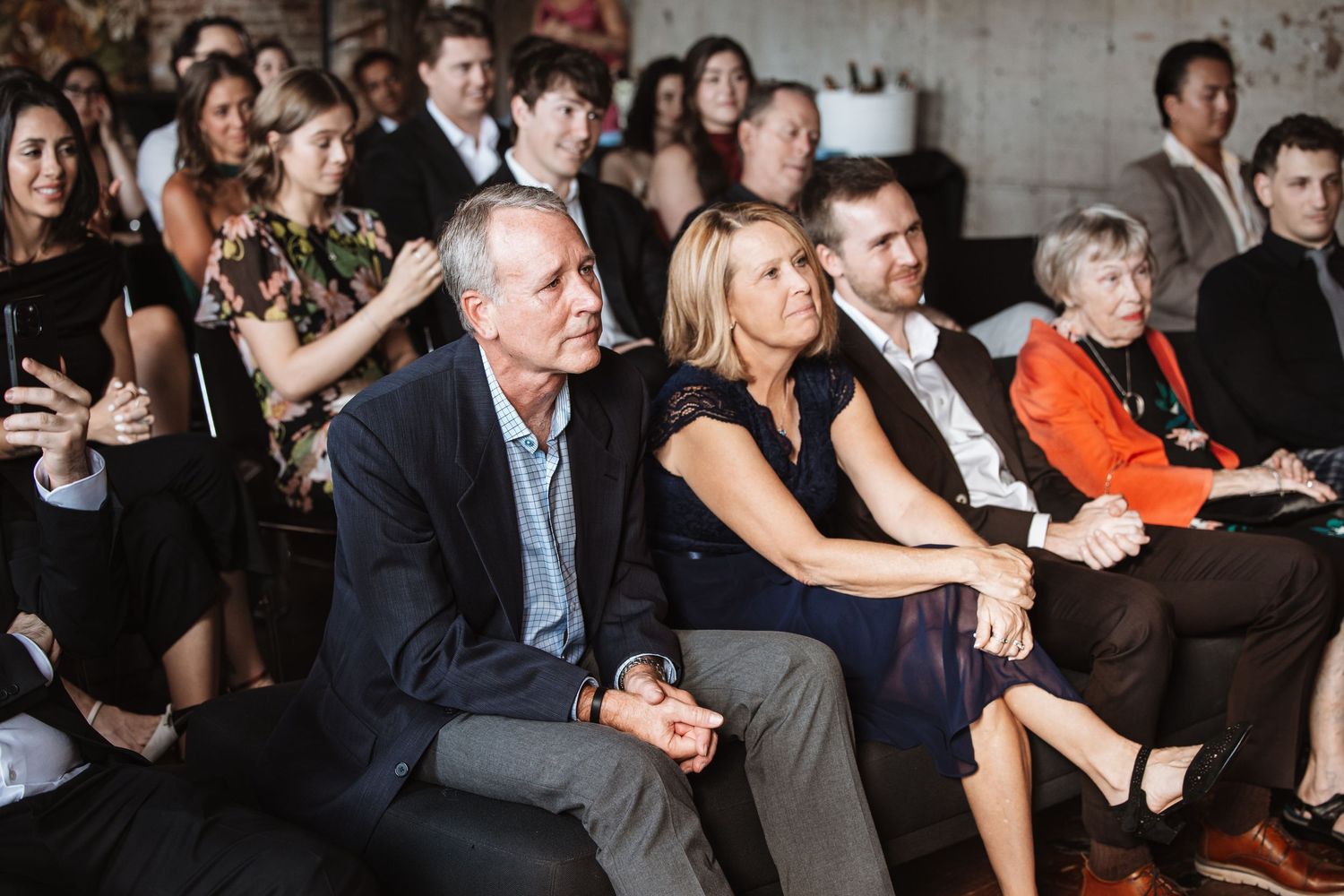 Guests seated at an indoor event, including a couple in the foreground, attentively watching a presentation.
